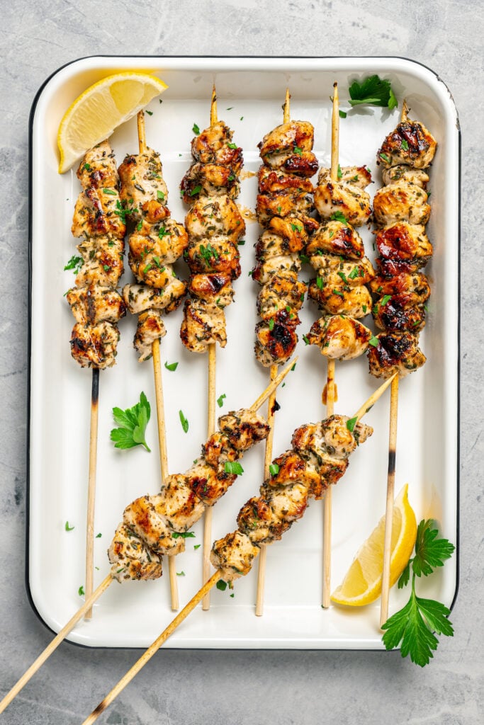 Grilled chicken on a stick, arranged on a tray with lemon slices.