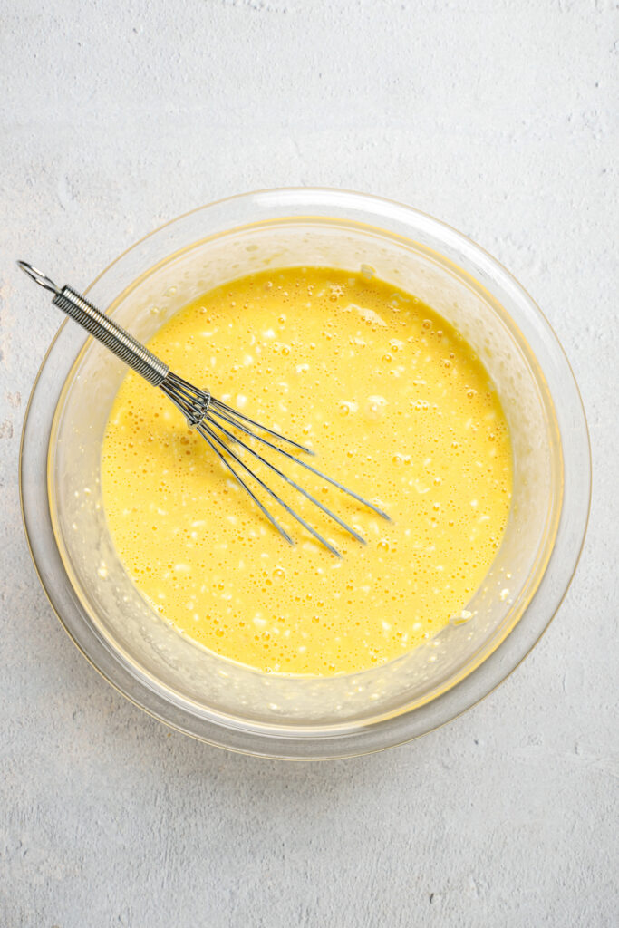 A yellow batter in a glass bowl with a whisk.