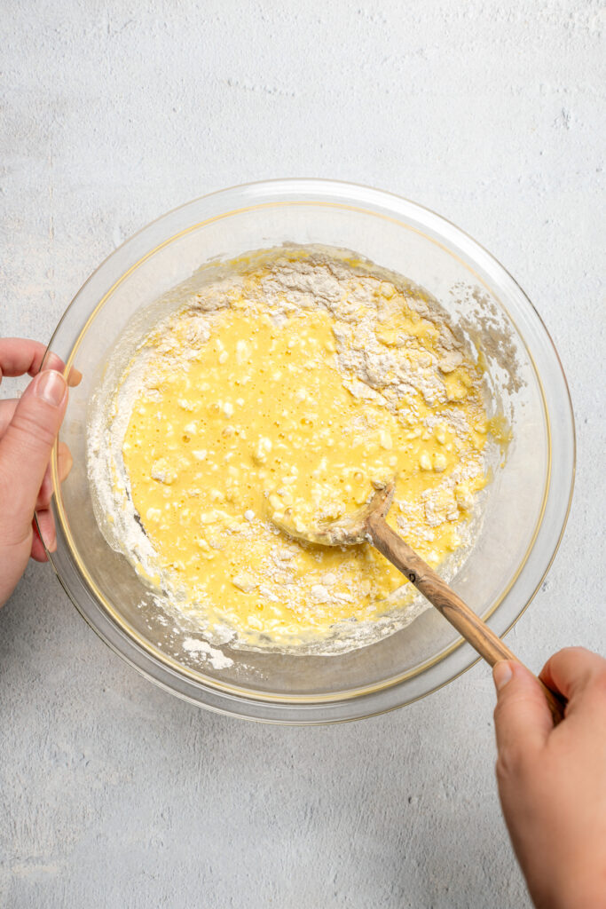 Incorporating dry ingredients into wet ingredients with a wooden spoon.