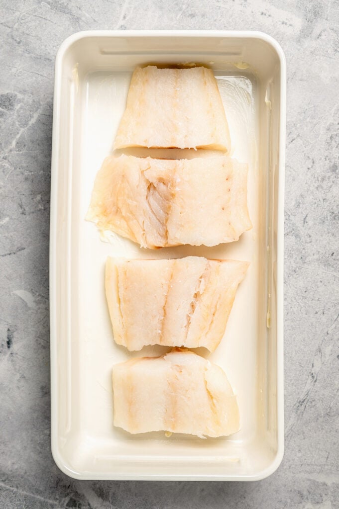 Pieces of fish laid in a row in a baking dish.