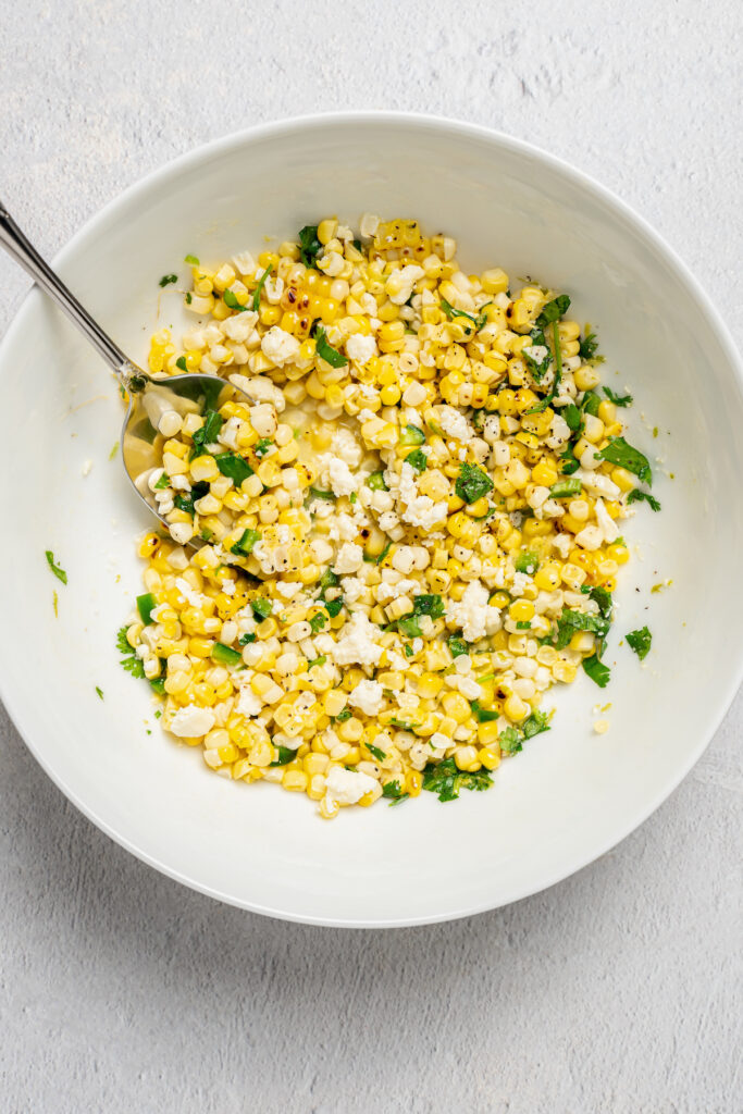 Mixing corn with the dressing ingredients.