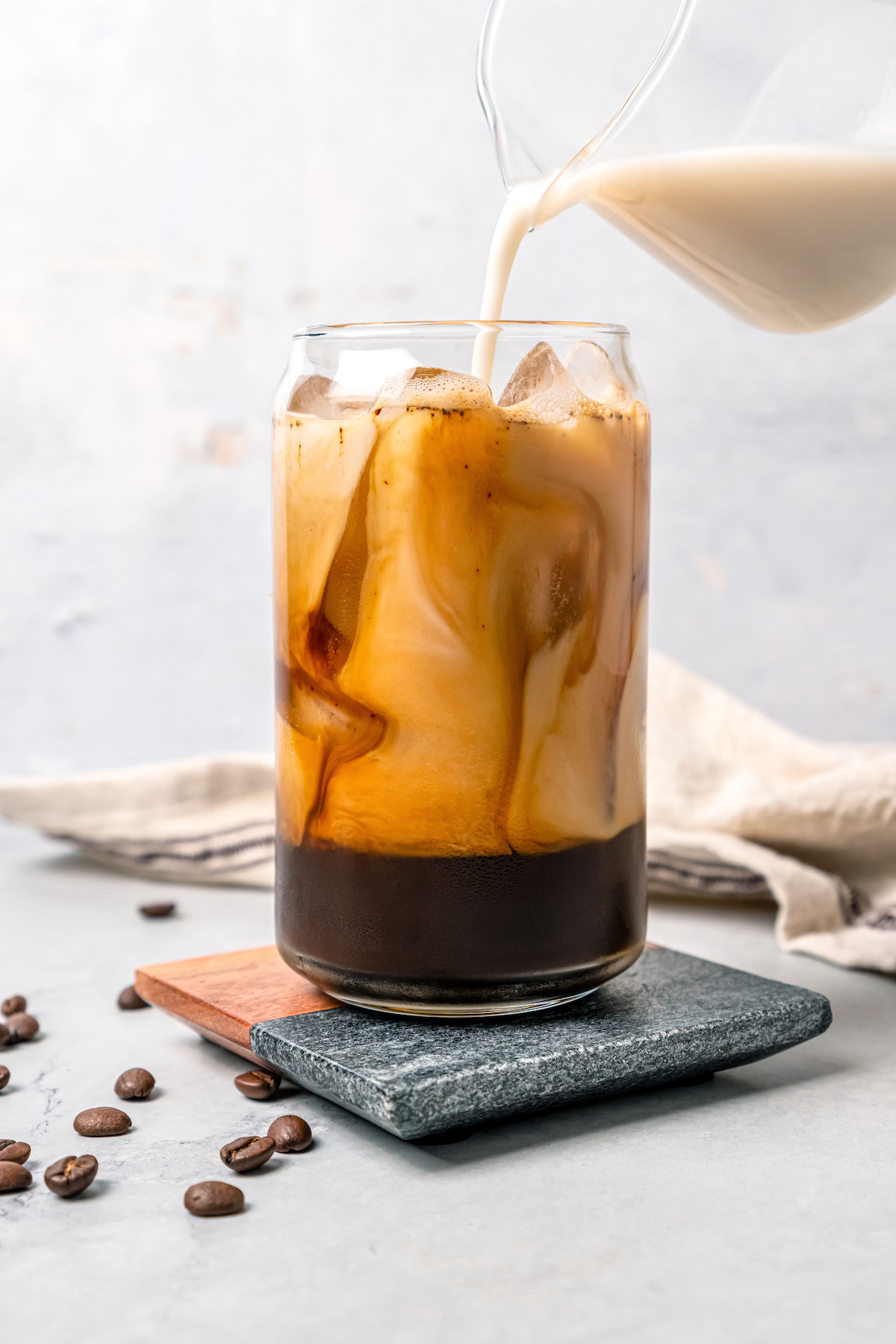 Adding milk to a glass of iced coffee.
