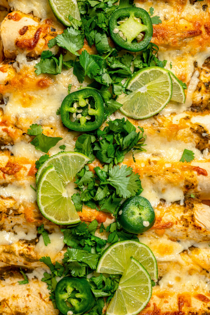 Close-up of enchiladas with cilantro, jalapeños, and lime wedges. 