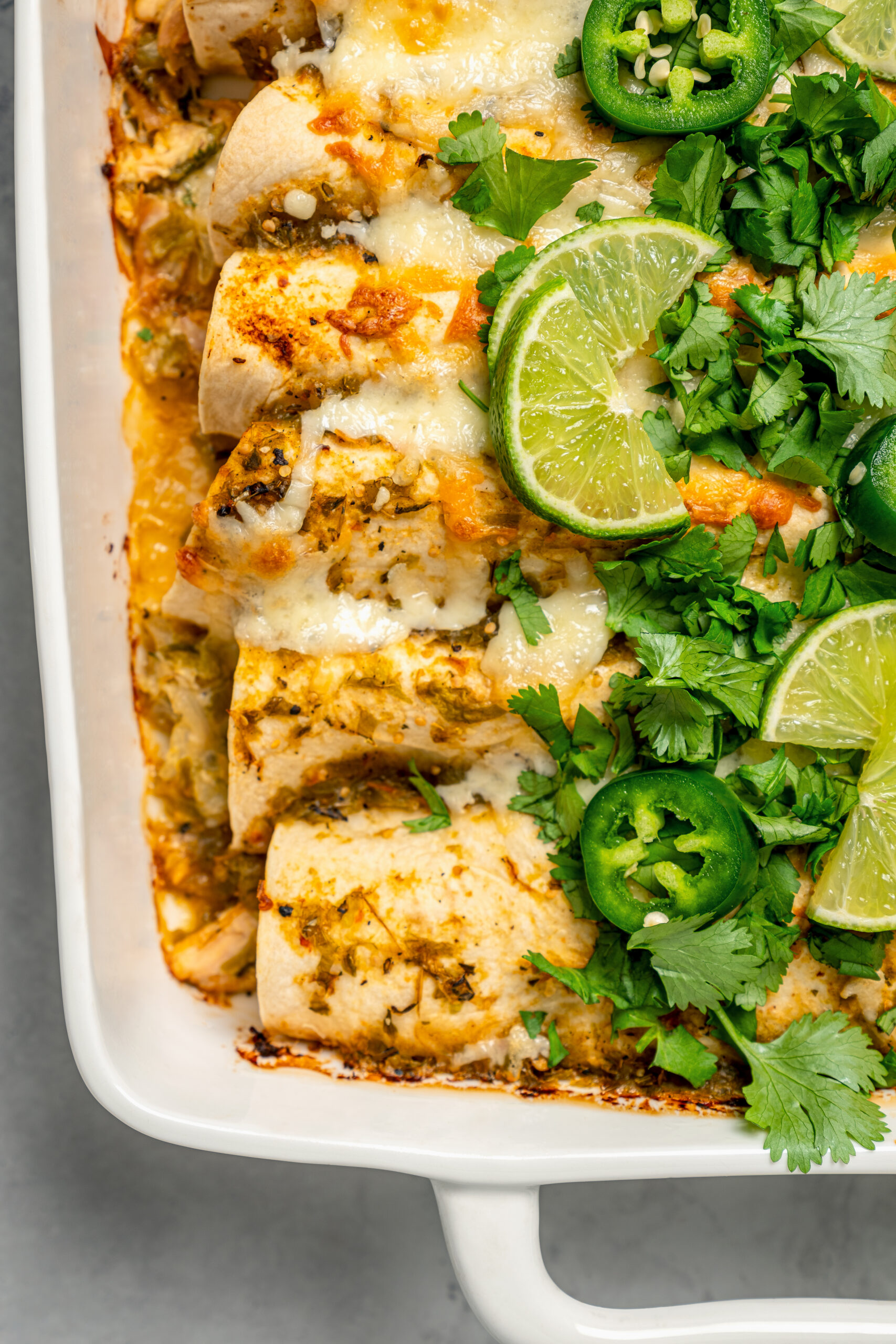 Close-up of enchiladas with lime wedges, cilantro, and jalapeños.